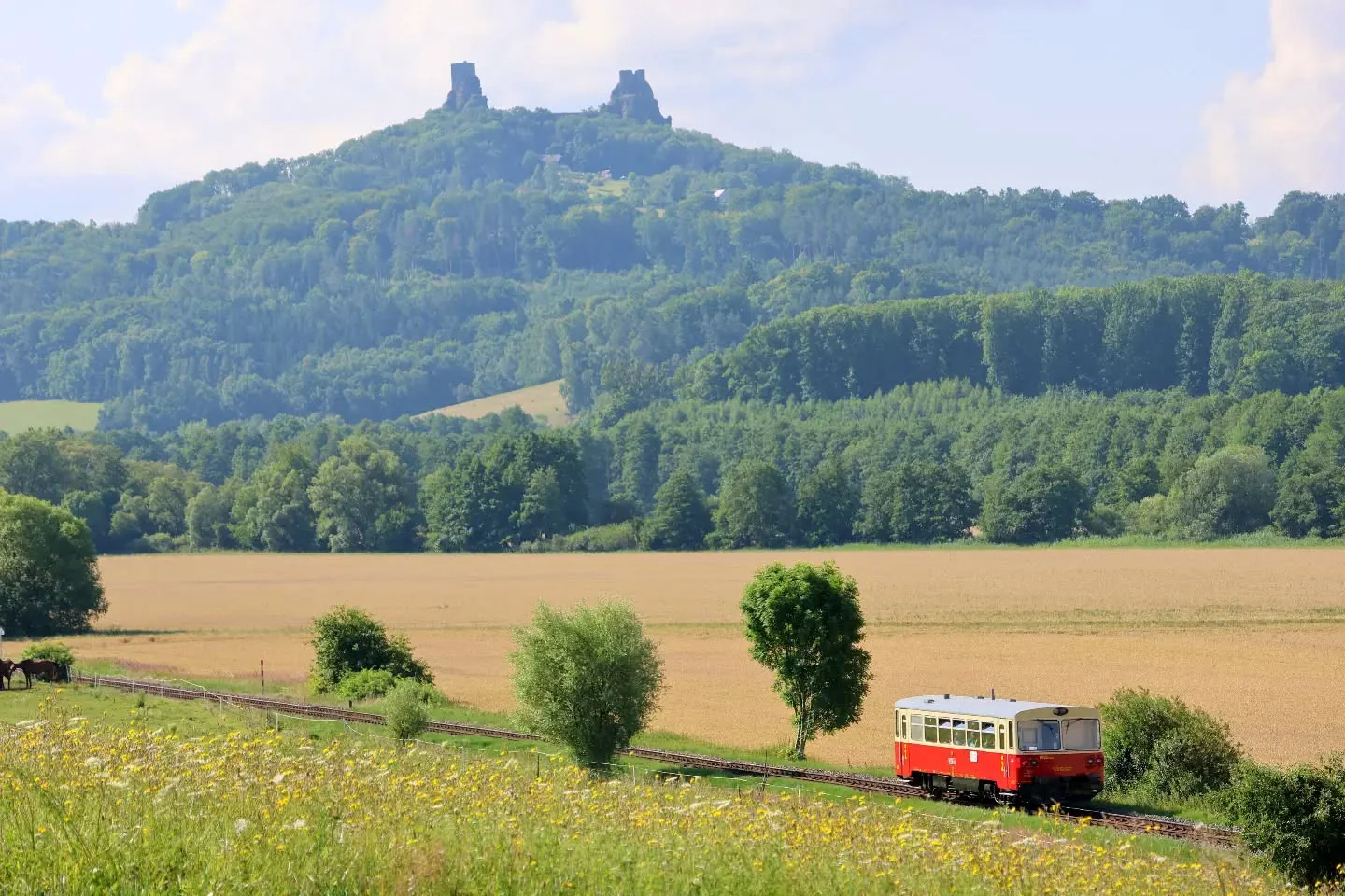 Historický motorový vůz M 152 projíždí krajinou pod hradem Trosky.